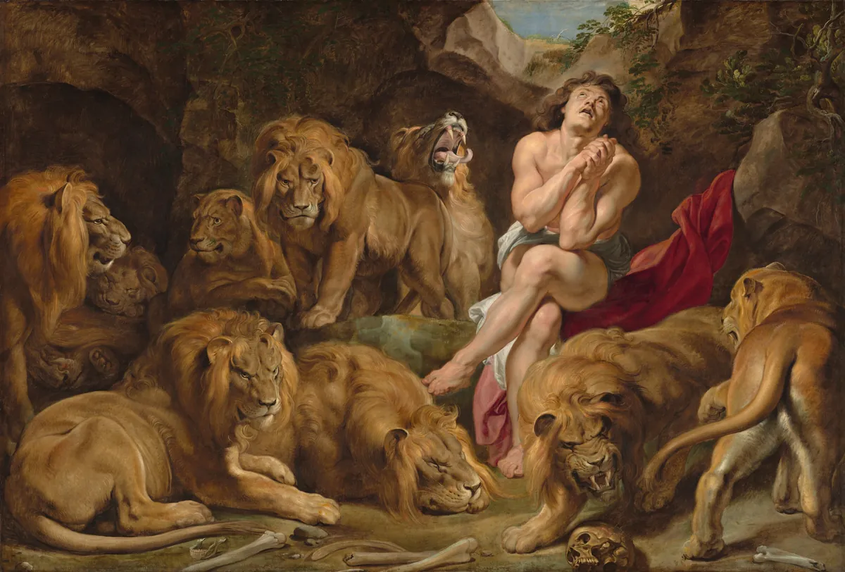 Rubens' Daniel in the Lions' Den: a nearly nude young man sits on a red cloak in a rocky pit, hands clasped and eyes raised toward light from an opening above, surrounded by nine life-size lions, with bones and a skull on the ground.